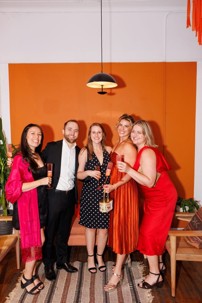 a group of guests pose together in front of an orange wall