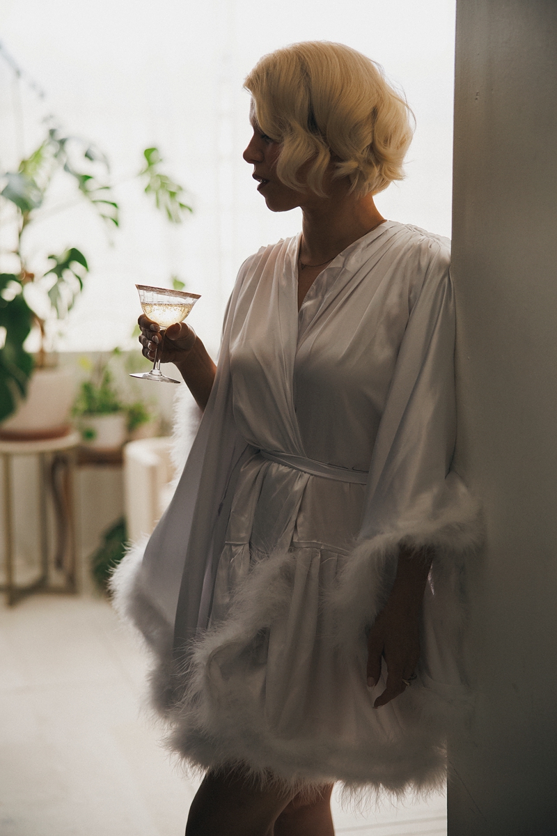 a bride stands in a doorway drinking champagne in a white robe in a chicago wedding venue
