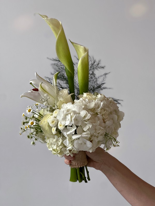 a white bridal bouquet is held against a white wall